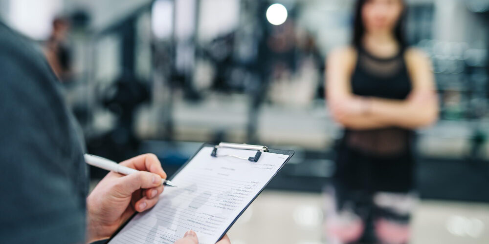 trainer-client-discussing-her-progress-gym-gym-instructor-writing-clipboard